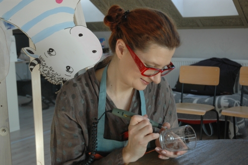 Knygų mugėje dailininkė Sigutė Ach ant stiklo graviruos 'Aukštyn kojom' personažus. © Sandra Junevičiūtė